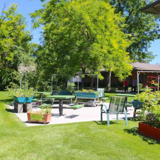 A sunny backyard garden with a patio area, surrounded by greenery and outdoor furniture.