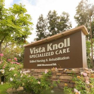 A sign for Vista Knoll Specialized Care, a skilled nursing and rehabilitation facility, surrounded by greenery.