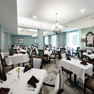 An elegant dining room with neatly arranged tables and chairs, featuring white tablecloths and a chandelier.