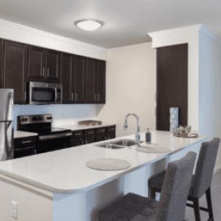 A modern kitchen with dark cabinets and stainless steel appliances, featuring a white countertop island with seating.