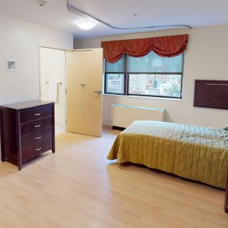 A simple bedroom with a single bed, dresser, and window with curtains.
