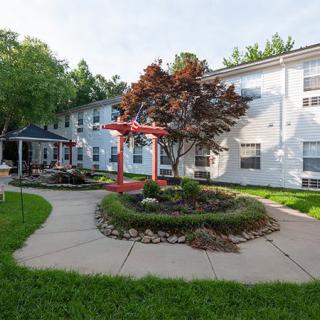 A well-maintained garden area outside a white residential building with a tree and seating area.