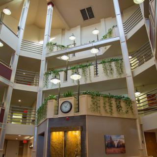 A modern atrium with multiple balconies, plants, and a central clock.