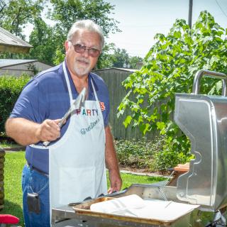 A man grilling food outdoors wearing an apron.