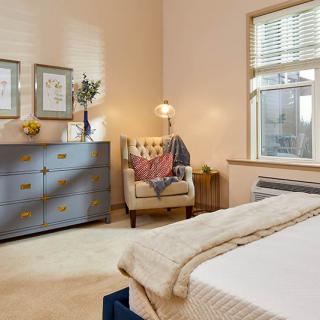 A cozy bedroom with a dresser, armchair, and soft lighting.