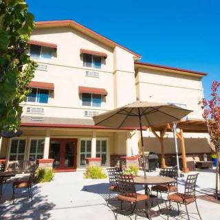 A sunny patio area with tables and umbrellas outside a multi-story building.