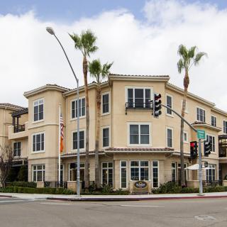 A modern residential building at a street intersection, surrounded by palm trees.