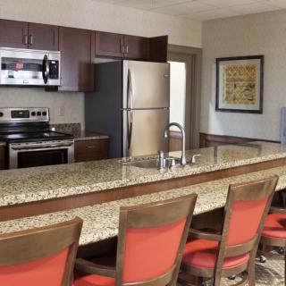 A modern kitchen interior with stainless steel appliances and a long granite countertop lined with red bar stools.