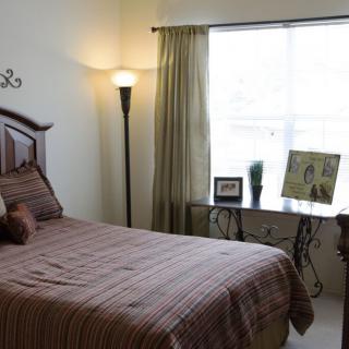 A cozy bedroom with a bed, floor lamp, and window letting in natural light.