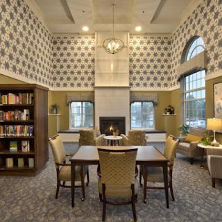 A cozy library space featuring comfortable seating and shelves filled with books, illuminated by natural light through large windows.