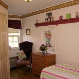 A cozy bedroom with a striped bedspread, a dresser with decor, and a comfortable chair by the window.