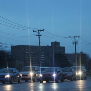 Evening traffic on a city street with cars lined up and buildings in the background.