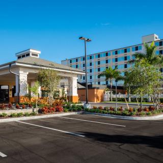 A modern hotel building with a well-maintained parking lot, surrounded by palm trees on a sunny day.