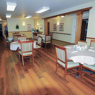 An empty dining room with neatly arranged tables and chairs, featuring a wooden floor.