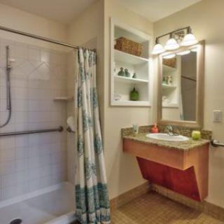 A cozy bathroom featuring a walk-in shower with a curtain, a sink with an overhead mirror, and neatly arranged shelves.