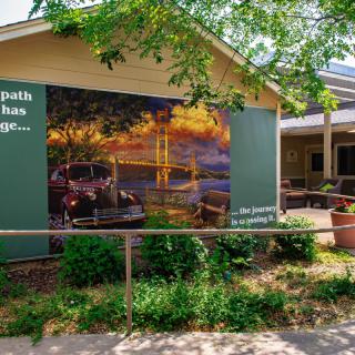A building exterior featuring a mural depicting a scenic landscape, surrounded by greenery.