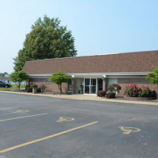A view of a brick building with landscaped areas and parking spaces in front.