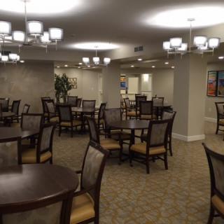 A spacious dining area with multiple tables and chairs, illuminated by elegant chandeliers.