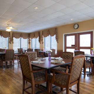 A cozy dining area featuring wooden tables and chairs, with ample natural light from large windows.