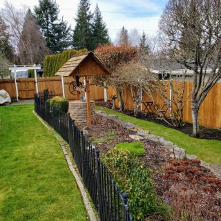 A well-maintained garden with a neat fence, green lawn, and various trees and shrubs.