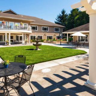 A sunny courtyard with a fountain, surrounded by patio furniture and a two-story building.