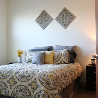 A cozy bedroom with patterned bedding, decorative pillows, and wall art above the bed.
