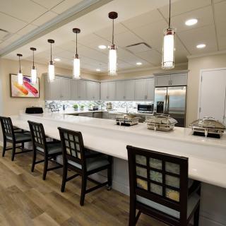 A modern kitchen with a long countertop, pendant lights, and seating area.