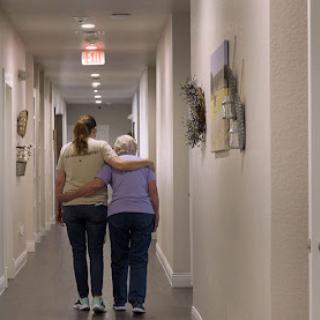A caregiver gently assists an elderly woman down a quiet hallway, showcasing the importance of support and companionship.