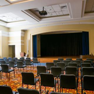 An empty auditorium with rows of chairs facing a stage.
