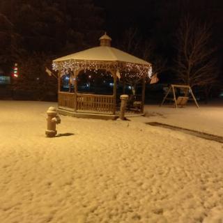 A peaceful winter scene featuring a snow-covered gazebo and outdoor swing under the night sky.