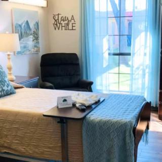 A well-decorated hospital room featuring a comfortable bed near a window, with a cushioned chair and soothing decor.