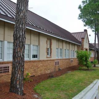 A single-story brick building with multiple windows, surrounded by trees and a well-maintained lawn.