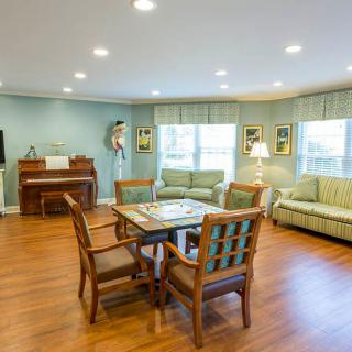 A cozy living room with hardwood floors, featuring a table and chairs, two couches, a piano, and decorative elements.