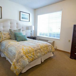 A cozy bedroom with a neatly made bed and natural light streaming through the window.
