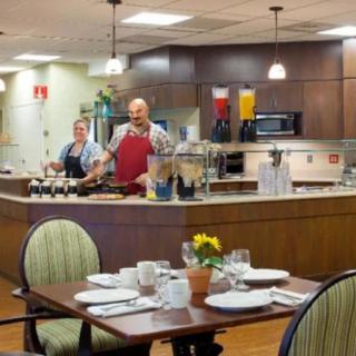 Chefs preparing food in a restaurant kitchen with neatly set tables in the foreground.