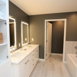 A modern bathroom with a double sink vanity, illuminated mirrors, and a bathtub.