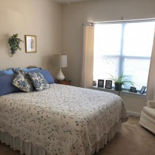 Cozy bedroom with a neatly made bed, a bedside lamp, and a window letting in natural light.