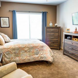 A cozy bedroom with a bed, dresser, and window with blue curtains.
