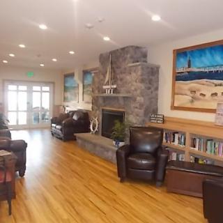A cozy living room with a stone fireplace, leather chairs, wooden floors, and artwork on the walls.