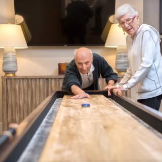 An elderly couple enjoying a game of shuffleboard indoors.