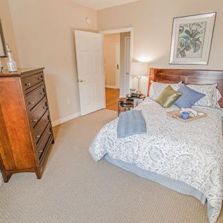 A cozy bedroom with a neatly made bed, wooden dresser, and soft lighting.