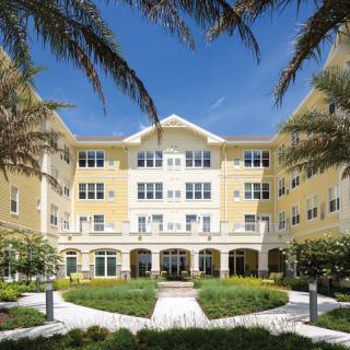 A residential building surrounded by palm trees and a well-maintained garden.
