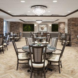An elegant dining room with modern decor, featuring multiple tables and chairs under a chandelier.