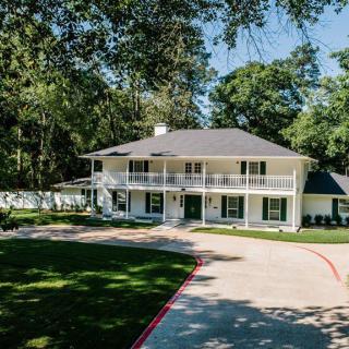 A two-story residential house with a spacious driveway surrounded by trees and greenery.