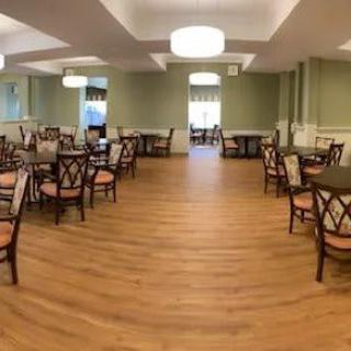 An empty dining room with arranged tables and chairs, featuring wooden flooring and elegant lighting.