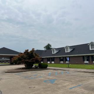 A view of a commercial building featuring a landscaped area and cloudy skies.