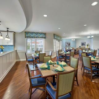 A cozy dining area with neatly arranged tables and chairs, featuring wood flooring and large windows.