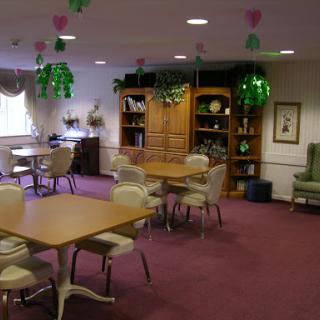 A cozy community room featuring tables, chairs, and decorative greenery.