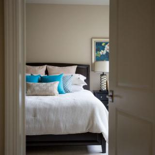 A cozy bedroom with a neatly made bed adorned with colorful pillows, viewed through an open door.