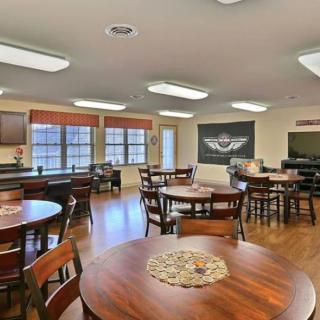 A cozy dining area with neatly arranged tables and chairs, featuring wooden flooring and ample natural light.